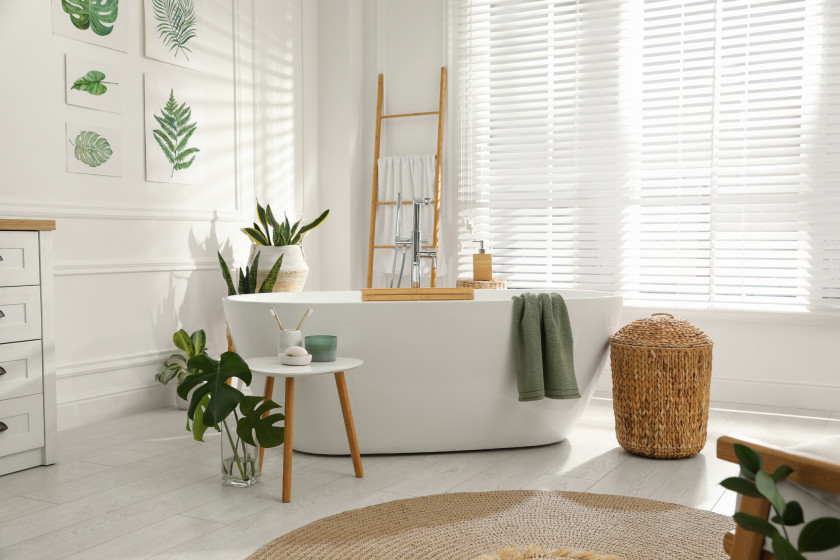 Badezimmer mit freistehender Wanne und weißen Jalousien vor großer Fensterfront