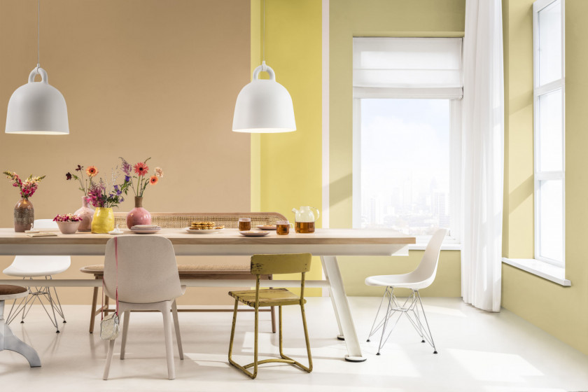 Esszimmer in warmen Pastelltönen mit einem massiven Esstisch aus Holz und bunt gemischten Stühlen