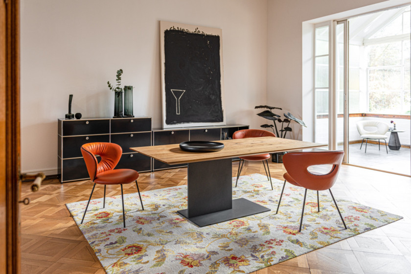 Esstisch MONOminal aus massiver Eiche mit einem Schwert aus pulverbeschichtetem Stahl in einem Esszimmer mit bequemen Lederstühlen in Orange und einem schwarzen USM Haller Sideboard